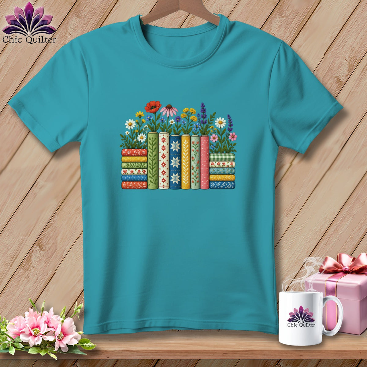 Teal t-shirt featuring a graphic of colorful patterned books and flowers on a wooden background.