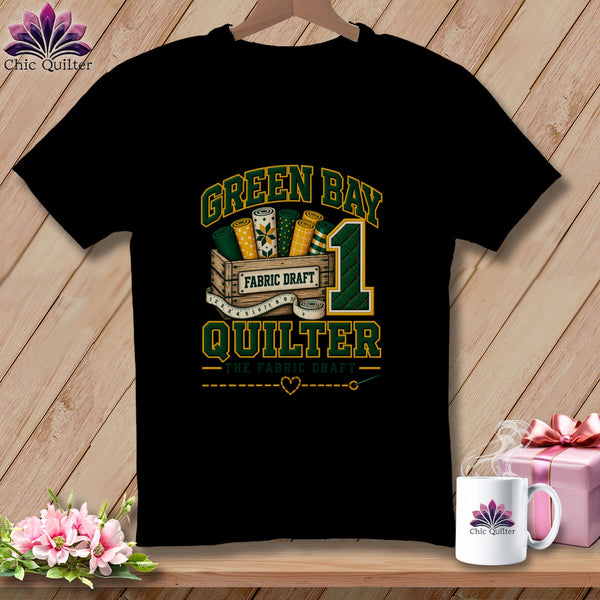 Black t-shirt featuring a green and gold "Green Bay Quilter" graphic with a wooden crate of fabric.