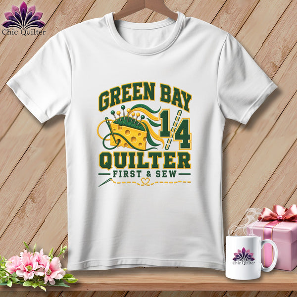 A white t-shirt hanging on a wooden background features a green and yellow Green Bay Quilter graphic.