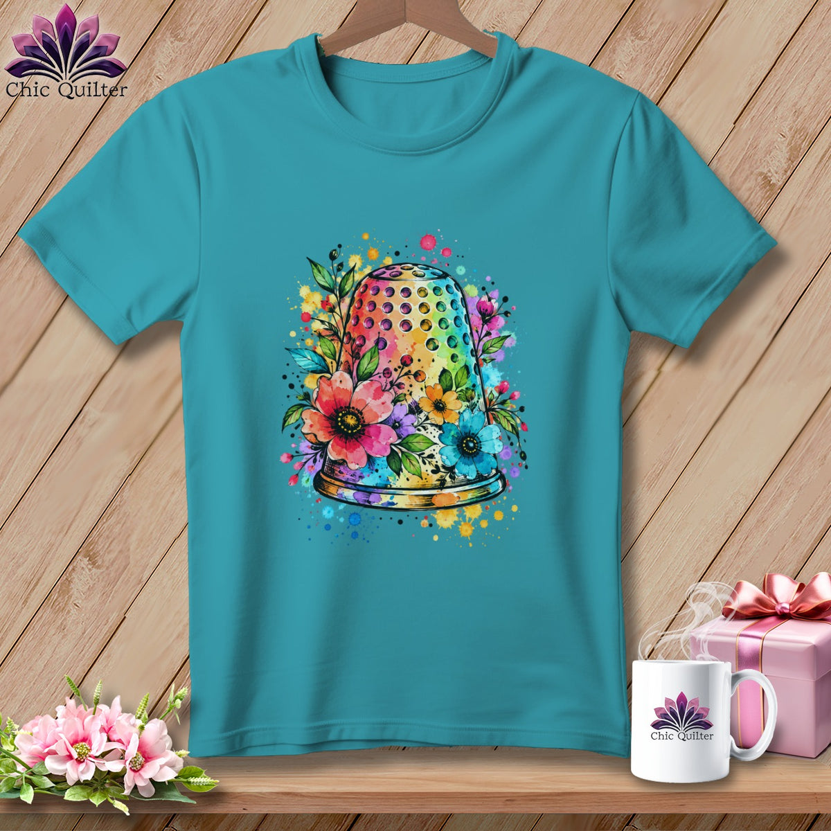 Teal crewneck t-shirt featuring a colorful watercolor graphic of a thimble surrounded by flowers.
