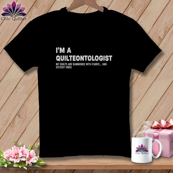 Black t-shirt with "I'M A QUILTEONTOLOGIST" and "MY QUILTS ARE SUMMONED WITH FABRIC... AND STITCHY VIBES" text.