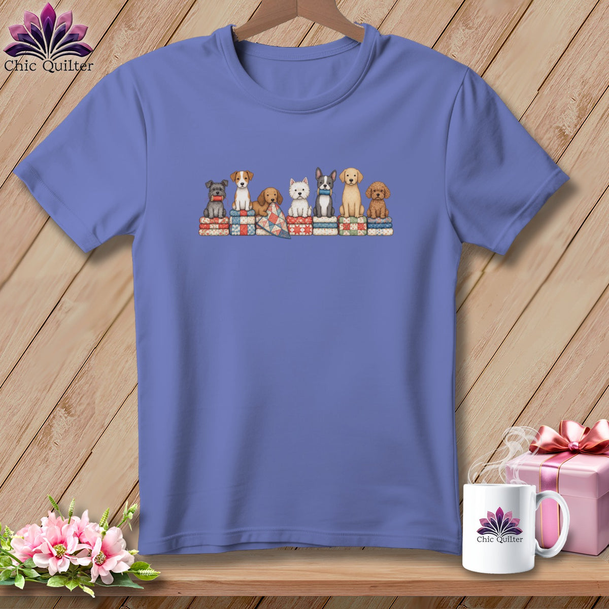 Periwinkle t-shirt featuring a graphic of seven cute puppies sitting atop colorful folded quilts.