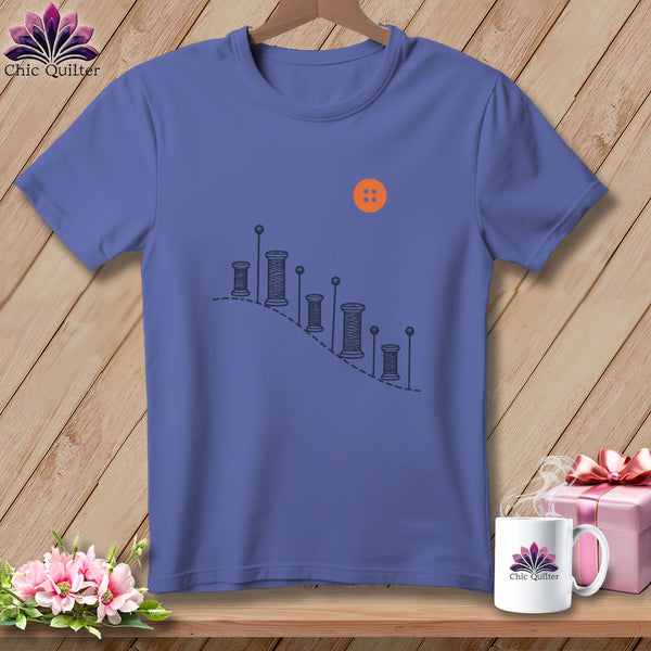 Purple t-shirt with spools of thread graphic and an orange button.