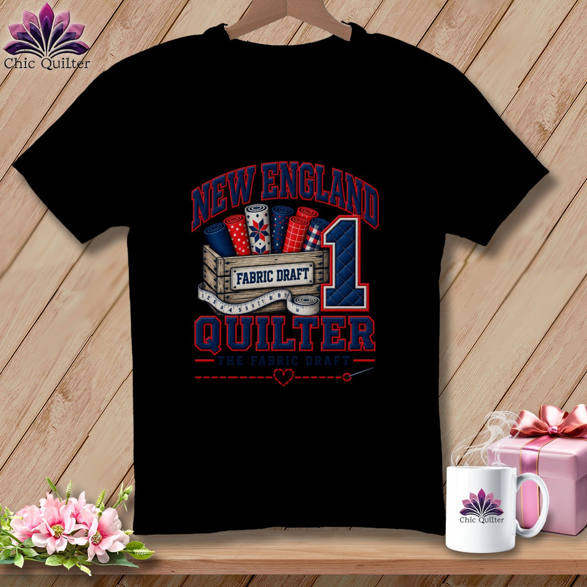 Black t-shirt featuring a New England Quilter graphic with fabric bolts, a wooden crate, and a large number one.