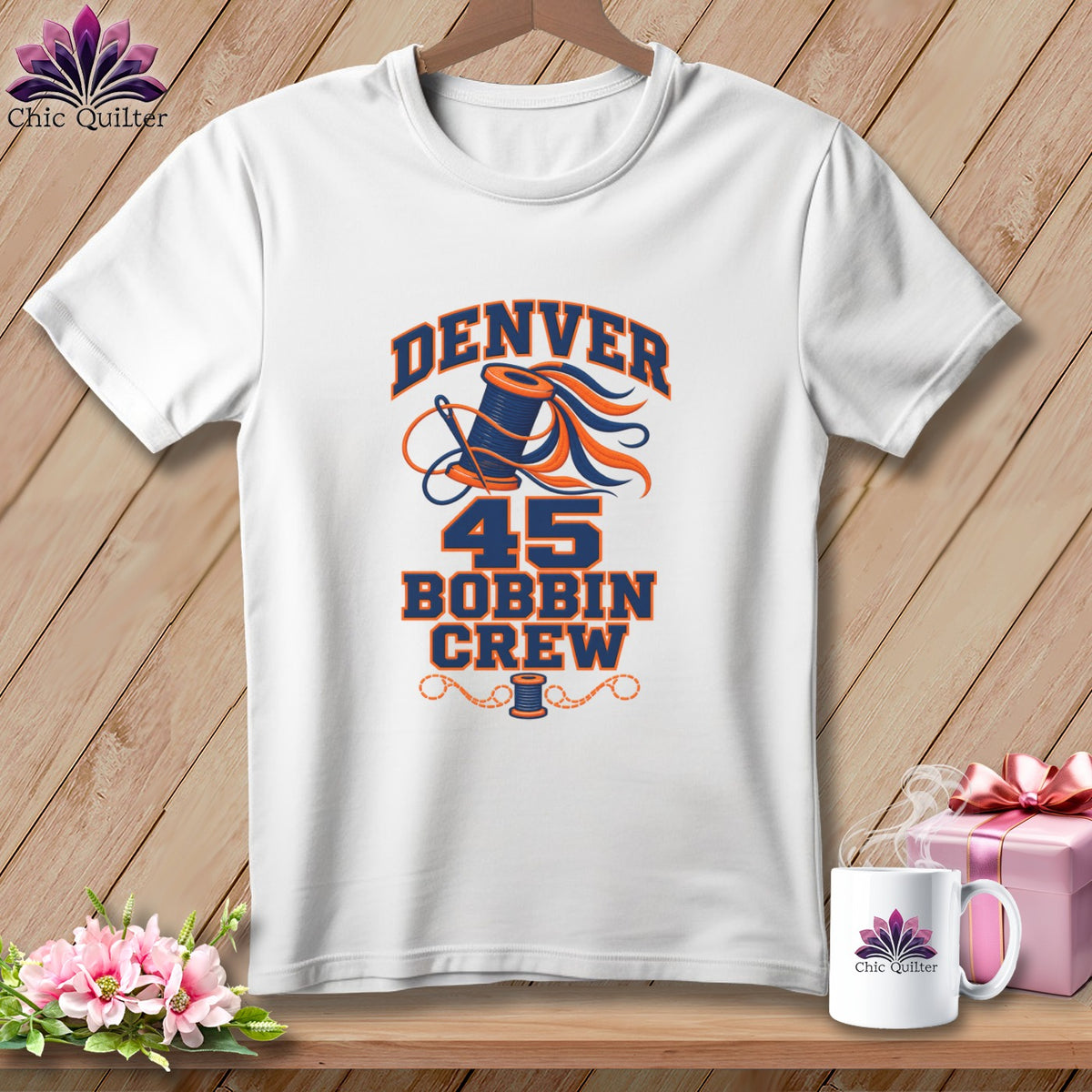 White crewneck t-shirt featuring a blue and orange Denver 45 Bobbin Crew graphic with thread and spool.