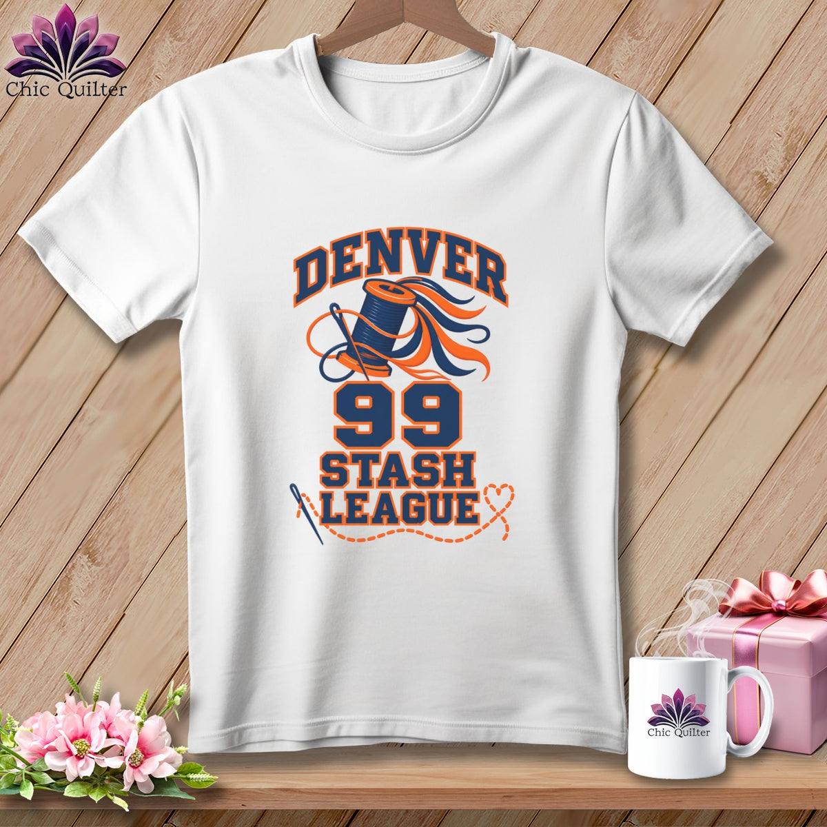 White t-shirt with a blue and orange Denver 99 Stash League quilting graphic on a wooden background.