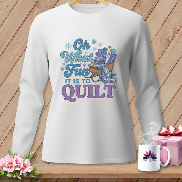 White long-sleeve shirt with "Oh What Fun It Is To Quilt" graphic and sleigh of fabrics.