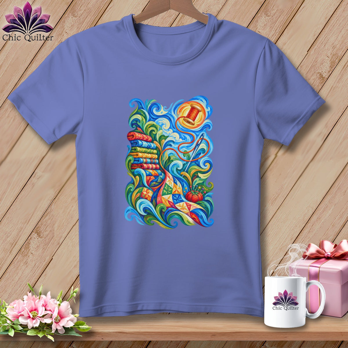 Purple short-sleeve t-shirt with a colorful graphic of sewing supplies, spools, and a patchwork quilt.