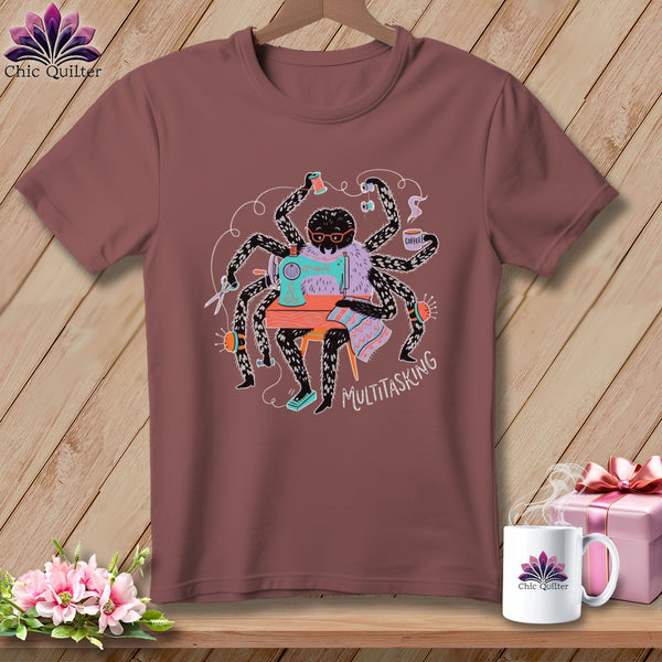 Spider sewing at a machine with text "MULTITASKING" on a maroon t-shirt.