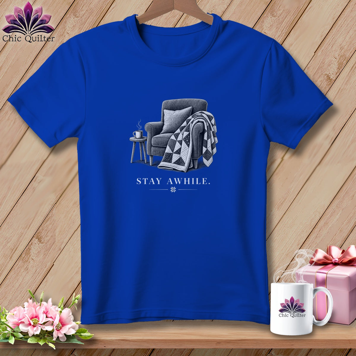 Royal blue t-shirt graphic with armchair, quilt, and text "STAY AWHILE."