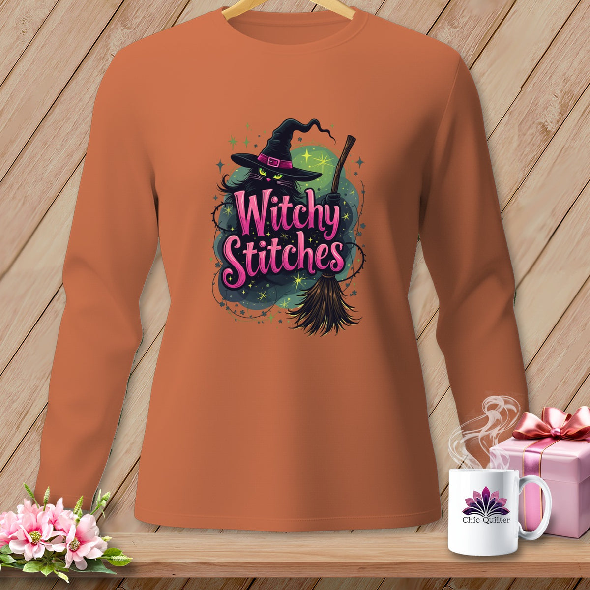 Orange long-sleeve shirt with a black cat in a witch hat holding a broom and text "Witchy Stitches".