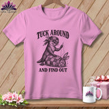 Pink t-shirt with a black graphic of an otter sewing a rabbit into a quilt, featuring the text Tuck Around And Find Out.