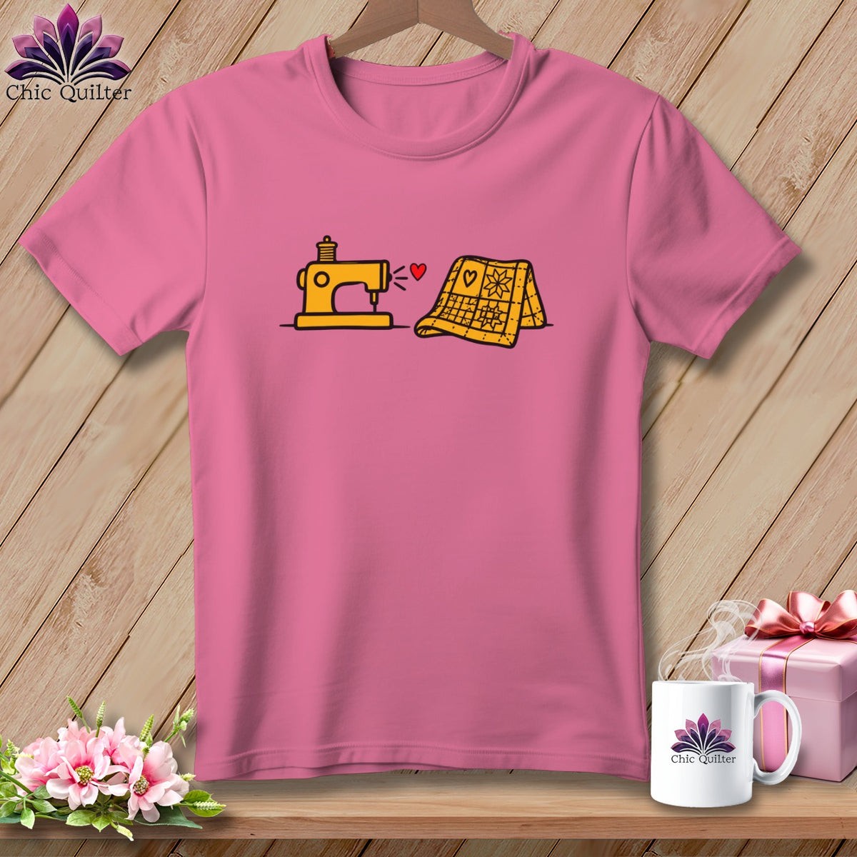 Pink t-shirt with a graphic of a yellow sewing machine, a red heart, and a folded yellow quilt.