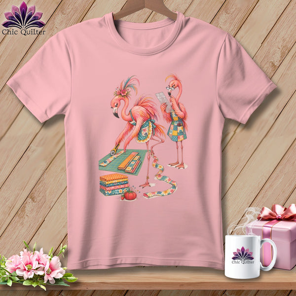 Pink t-shirt with two flamingos quilting, one cutting fabric and the other reading instructions.