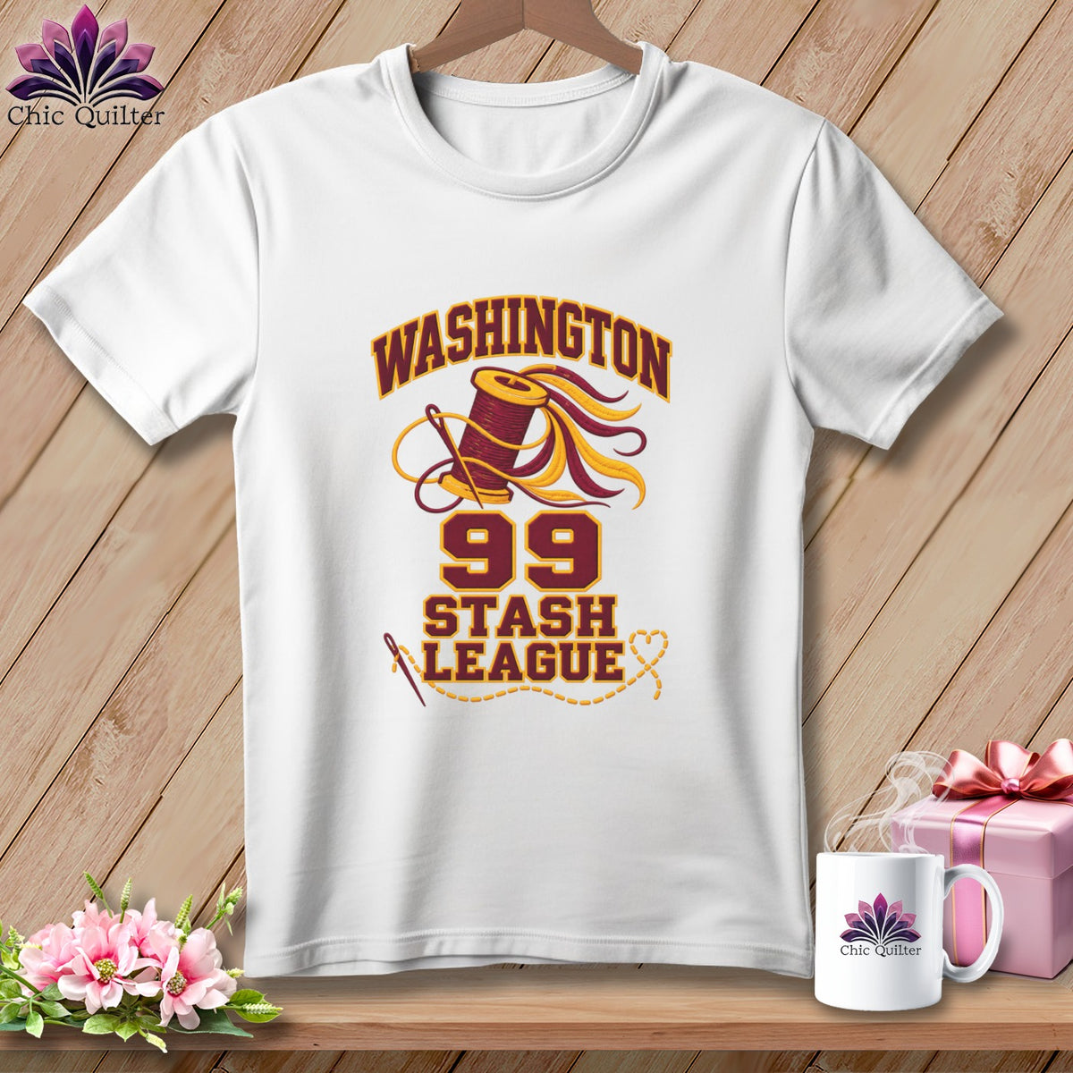 A white t-shirt hanging on a wooden background, featuring a sewing graphic with the text Washington 99 Stash League.