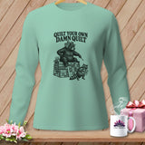 Mint green long-sleeve shirt featuring a black graphic of a bear and raccoon with the text Quilt Your Own Damn Quilt.
