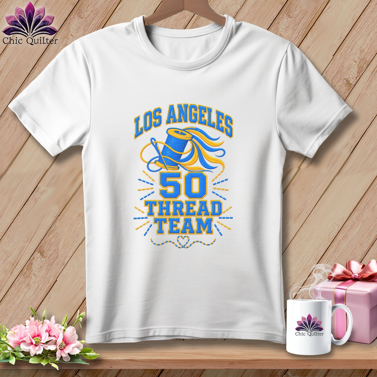 A white t-shirt hanging on a wooden background, featuring blue and yellow embroidery with the text "Los Angeles 50 Thread Team."