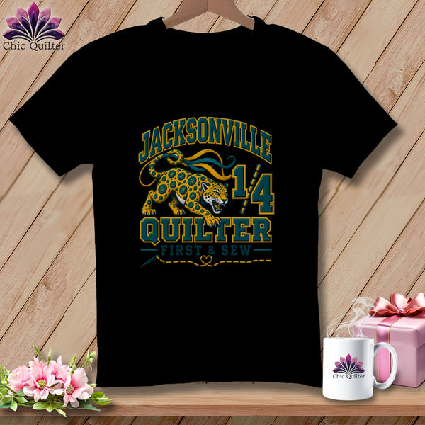 Black t-shirt featuring a Jacksonville Quilter graphic with a spotted cat, sewing tools, and text.