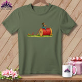 An olive green t-shirt featuring an illustration of a woman riding a large spool of red thread.