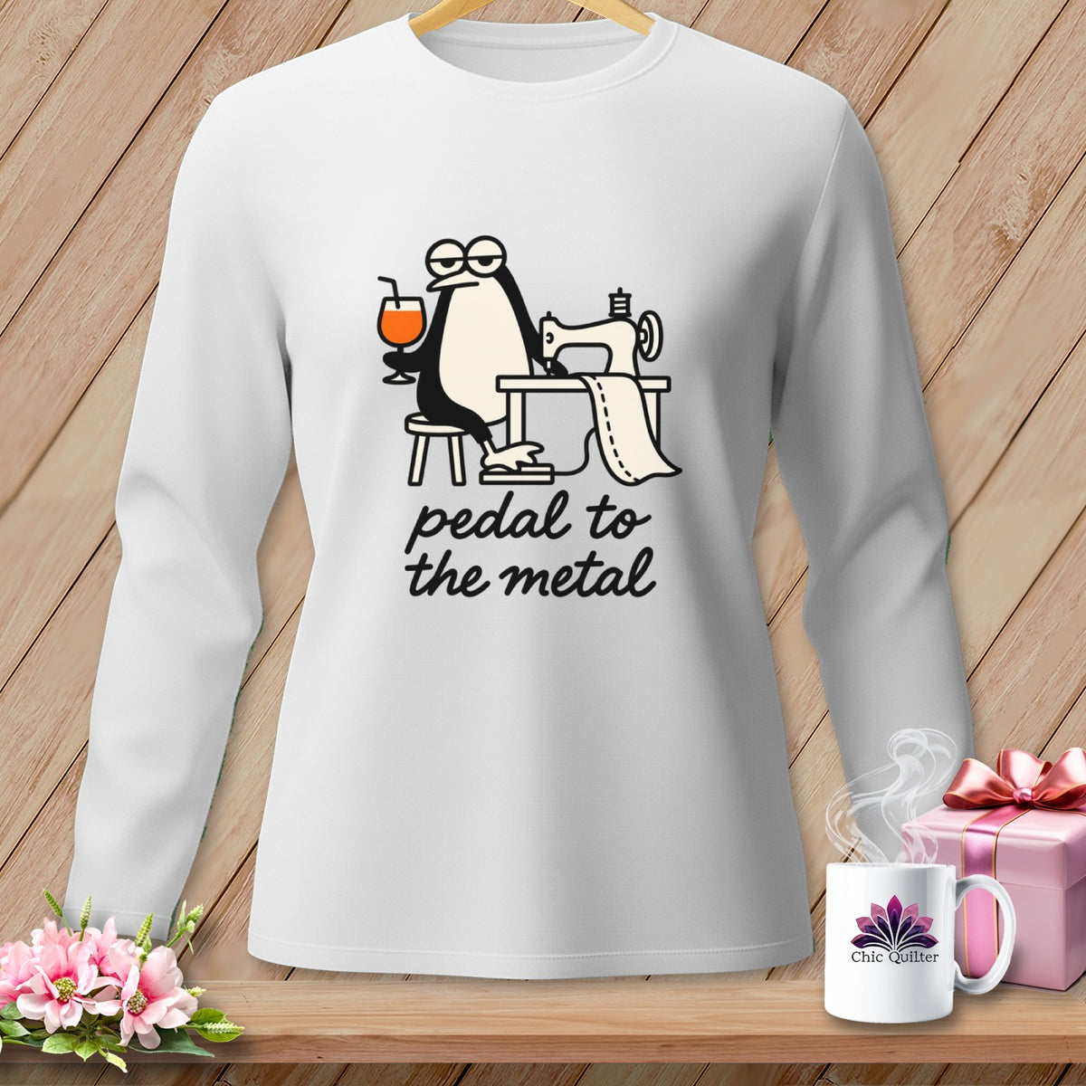 White long-sleeve shirt with penguin sewing, holding drink, and text "pedal to the metal."