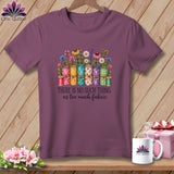 Mauve short-sleeve t-shirt with a colorful graphic of rolled fabric, flowers, and the text 