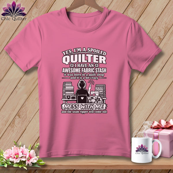 Pink t-shirt with text about being a spoiled quilter, graphic of a quilter, and white mug.