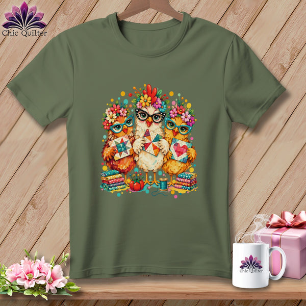 Olive green t-shirt featuring a graphic of three whimsical chickens wearing glasses and floral crowns while holding quilted blocks.