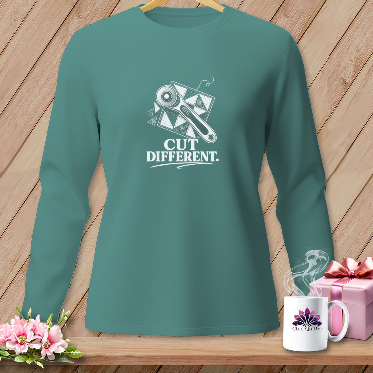 Teal long-sleeve shirt with rotary cutter and quilt block graphic and text "CUT DIFFERENT.".