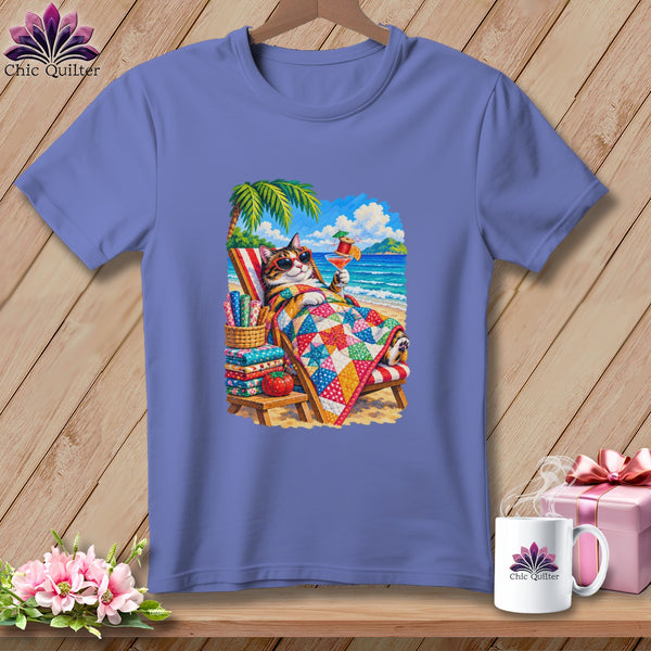 A periwinkle blue t-shirt with a graphic of a cat relaxing on a beach under a palm tree.