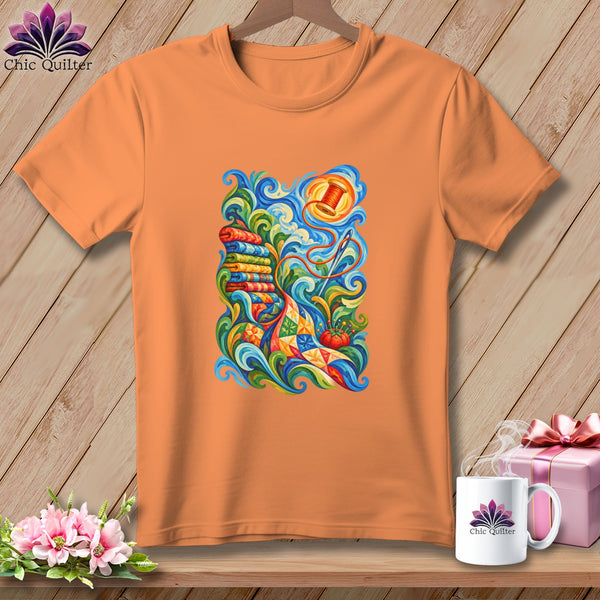 An orange crewneck t-shirt features a colorful, swirling quilting graphic on the front, displayed against a wooden background.