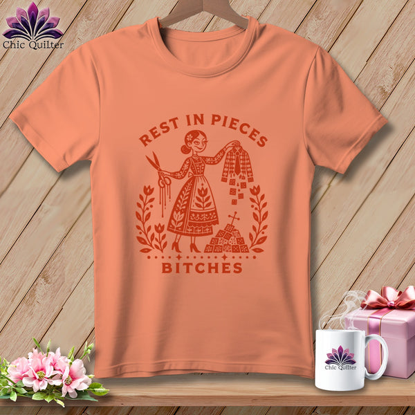 Peach t-shirt with "Rest in Pieces Bitches" graphic featuring a woman with scissors and fabric.
