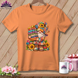 Orange t-shirt featuring a colorful gnome graphic holding a tall stack of folded fabrics, surrounded by sunflowers.