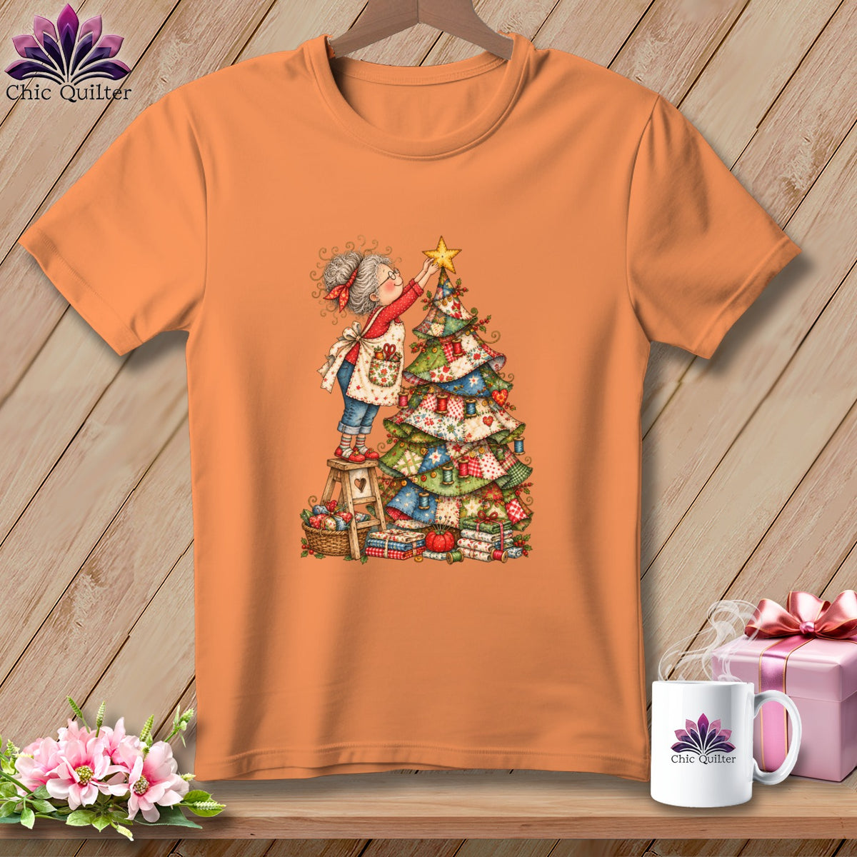 Orange t-shirt featuring a cartoon woman placing a star on a Christmas tree made of quilts.
