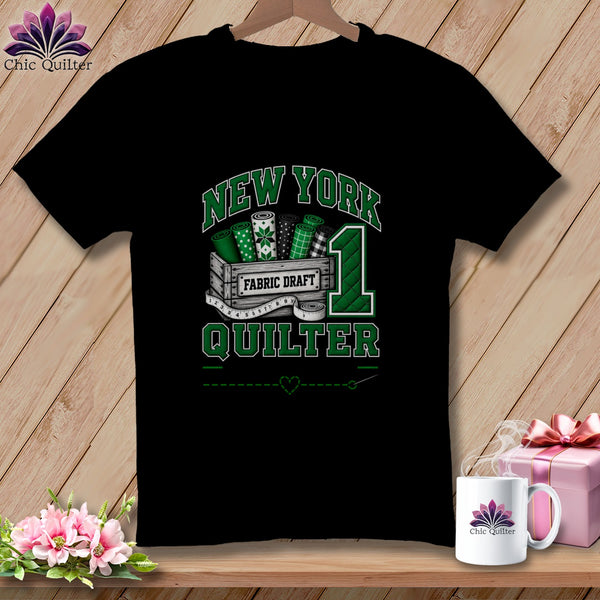 Black t-shirt featuring a green graphic with rolled fabric, a measuring tape, and text reading New York Quilter.