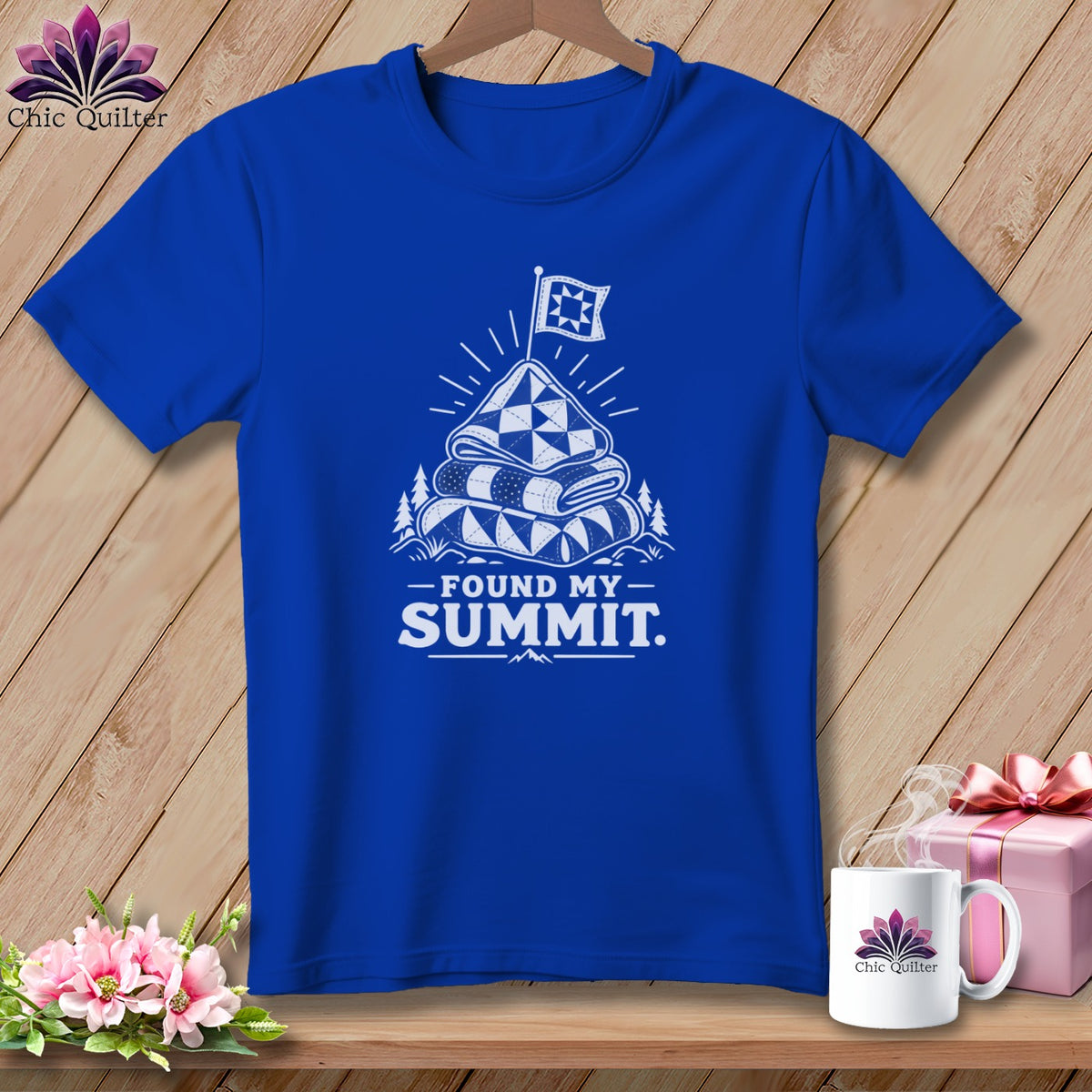 Blue t-shirt with white graphic of stacked quilts, flag, mountains, and text "FOUND MY SUMMIT."