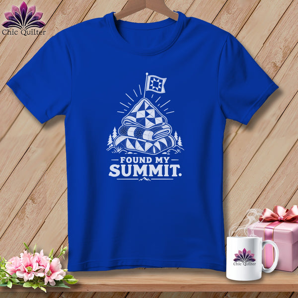 Blue t-shirt with white graphic of stacked quilts, flag, mountains, and text "FOUND MY SUMMIT."