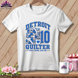 A white t-shirt features blue text reading DETROIT QUILTER and FIRST DOWN, SEW ON, alongside a stack of blue quilts, a coffee mug, and the number ten.