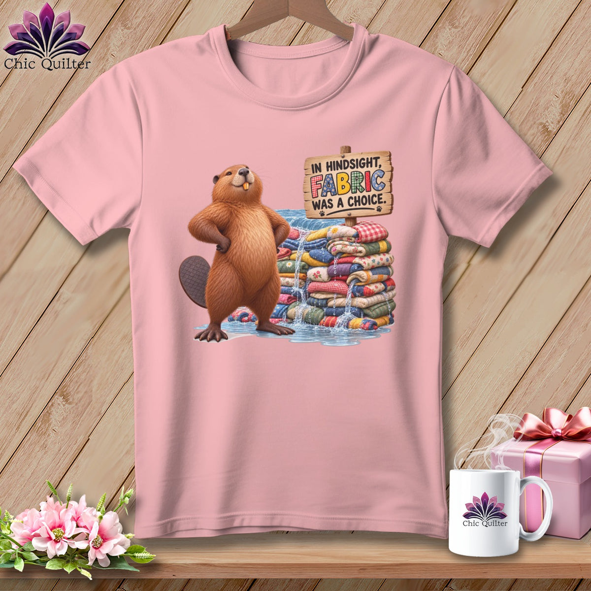 Pink t-shirt with a cartoon beaver standing next to fabric rolls with text.