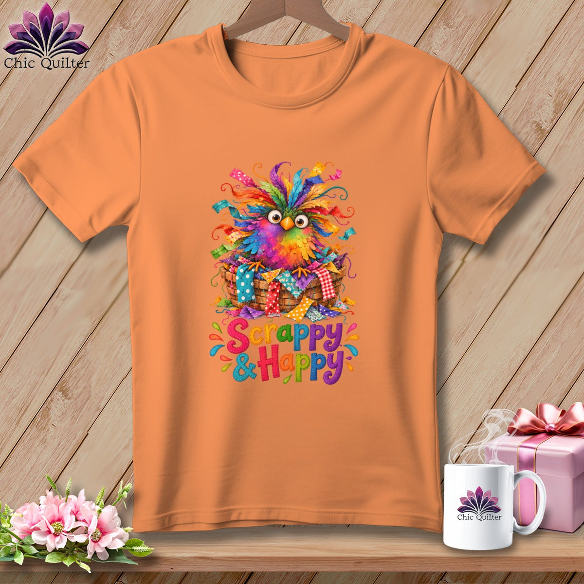 An orange crewneck t-shirt featuring a colorful bird in a basket and the text "Scrappy & Happy".