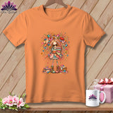 An orange crew neck t-shirt featuring a whimsical illustration of a sewing girl on a wooden background.