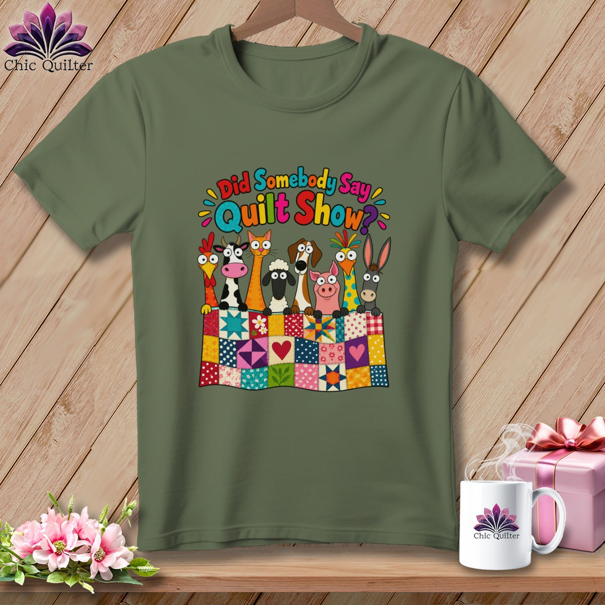 Olive green t-shirt with a graphic of cartoon farm animals behind a colorful quilt, featuring the text Did Somebody Say Quilt Show.