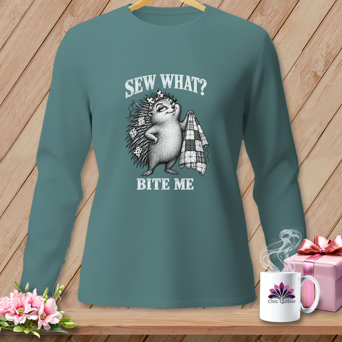 Teal long-sleeve shirt featuring a graphic of a hedgehog holding a quilt and text reading Sew What Bite Me.
