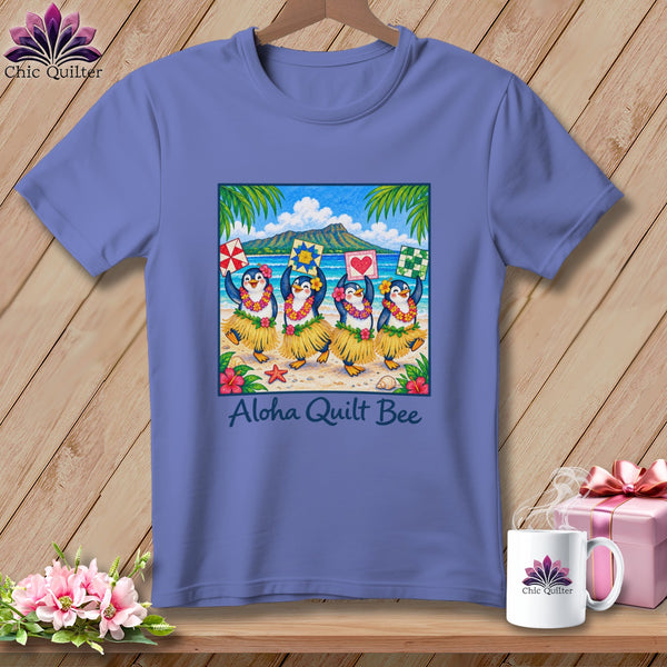 Blue t-shirt featuring a graphic of four penguins hula dancing on a beach with the text Aloha Quilt Bee.