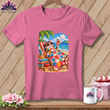 A pink t-shirt displays a graphic of a cat lounging on a beach under a palm tree with a colorful quilt and a cocktail.