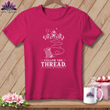 Pink t-shirt with white design of a spool of thread and mountains, text 