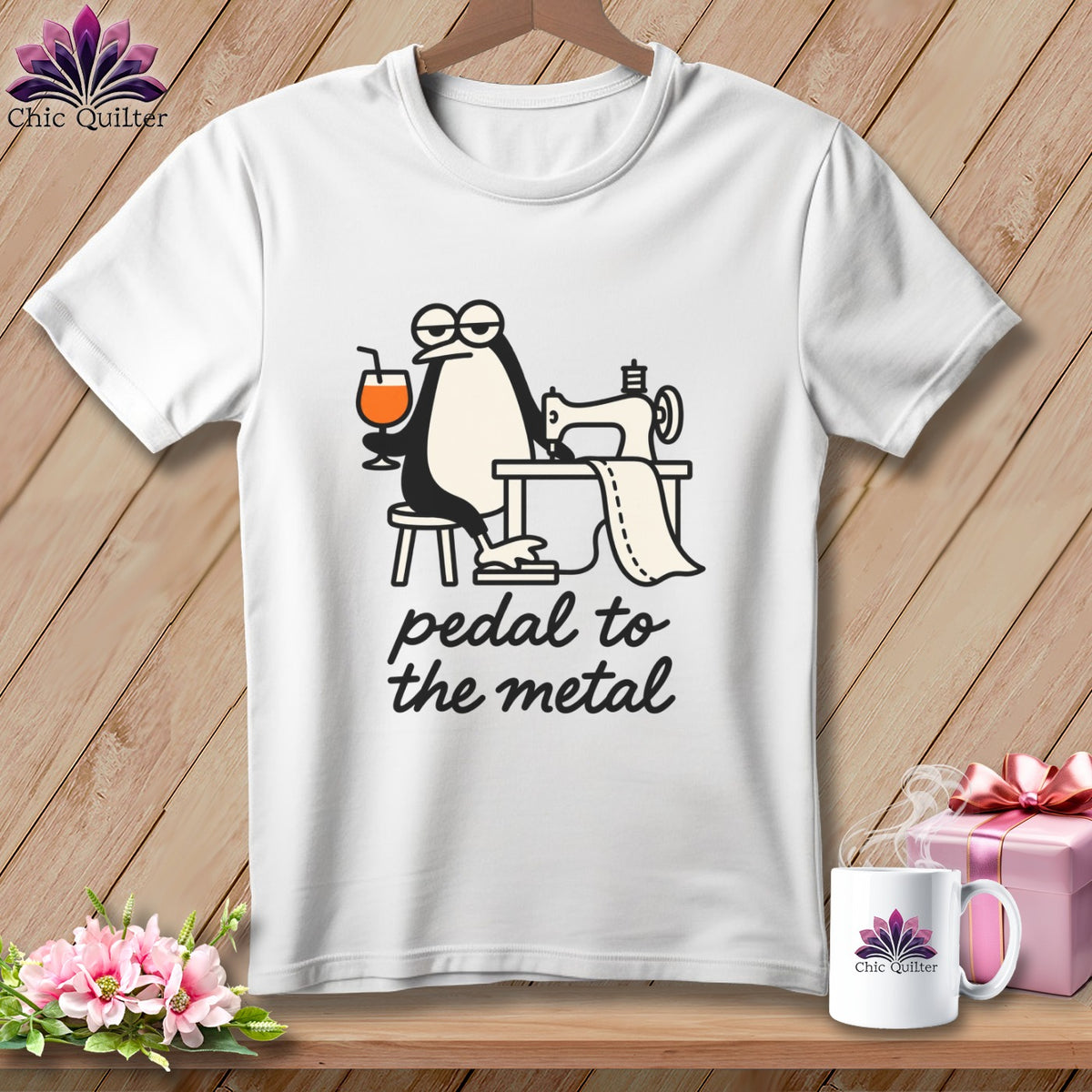 White t-shirt with a cartoon penguin sewing and the text "pedal to the metal".