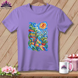 A purple crewneck t-shirt hangs against a wooden wall, featuring a colorful sewing-themed graphic on the front.