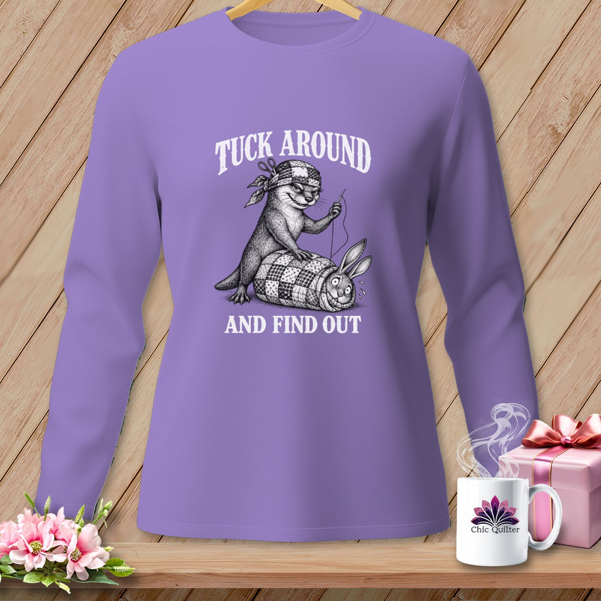 A purple long-sleeve shirt featuring a black-and-white graphic of an otter sewing a rabbit into a quilt, with the text TUCK AROUND AND FIND OUT.
