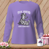 A purple long-sleeve shirt featuring a black-and-white graphic of an otter sewing a rabbit into a quilt, with the text TUCK AROUND AND FIND OUT.