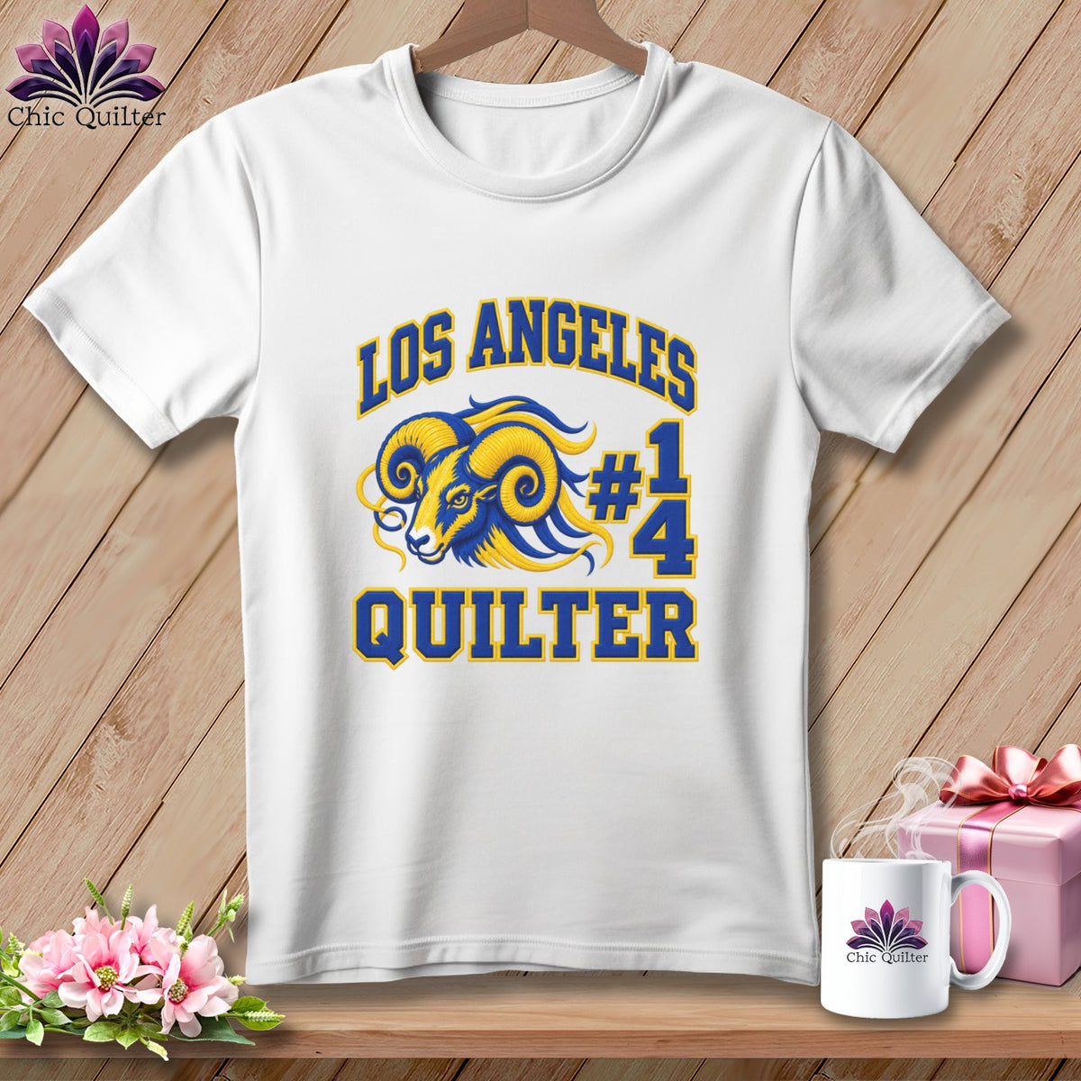White short-sleeve t-shirt with blue and yellow Los Angeles Quilter ram graphic on wooden background.